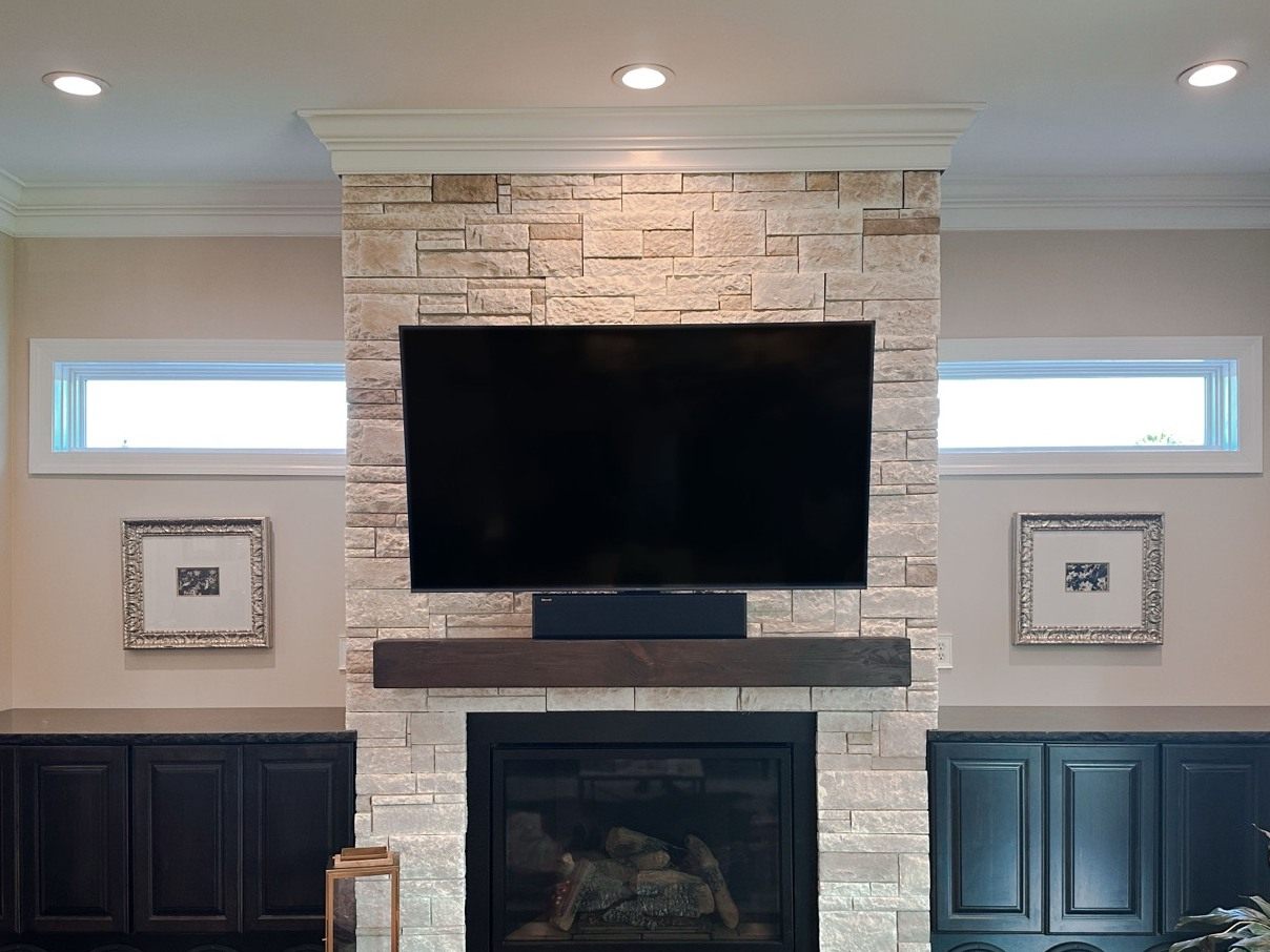 TV mounted on a stone fireplace with a soundbar, concealed wiring, and subwoofers built into the flanking cabinets