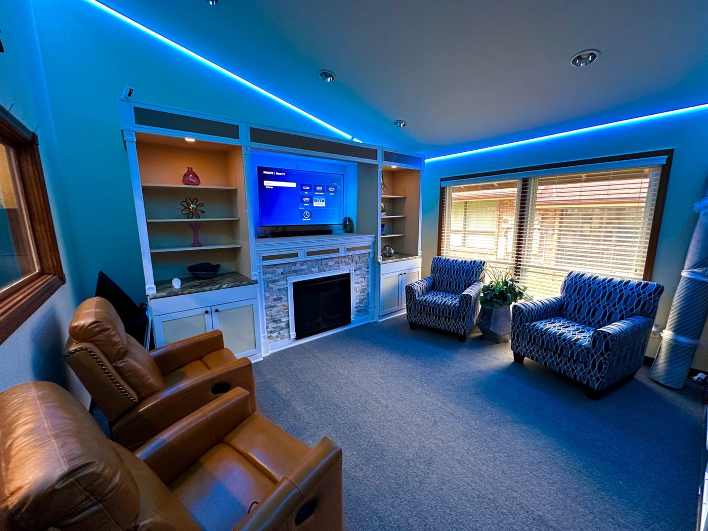Finished media room with the TV switched on, recliners facing the screen, and tunable LED cove lighting around the ceiling