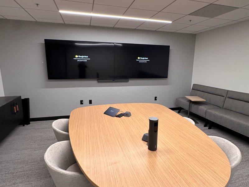 Boardroom with dual wall-mounted displays, a soundbar, and an oval conference table
