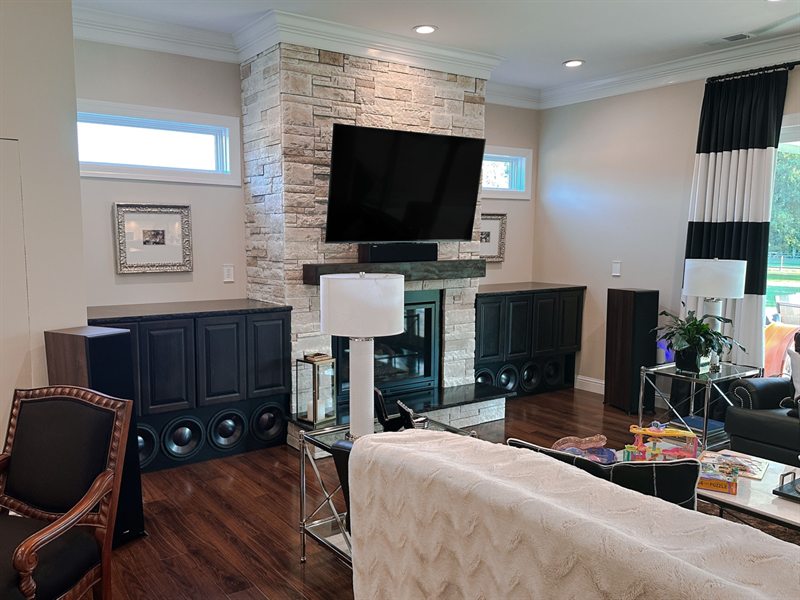 Living room TV mounted above a stone fireplace with subwoofers in the built-in cabinets