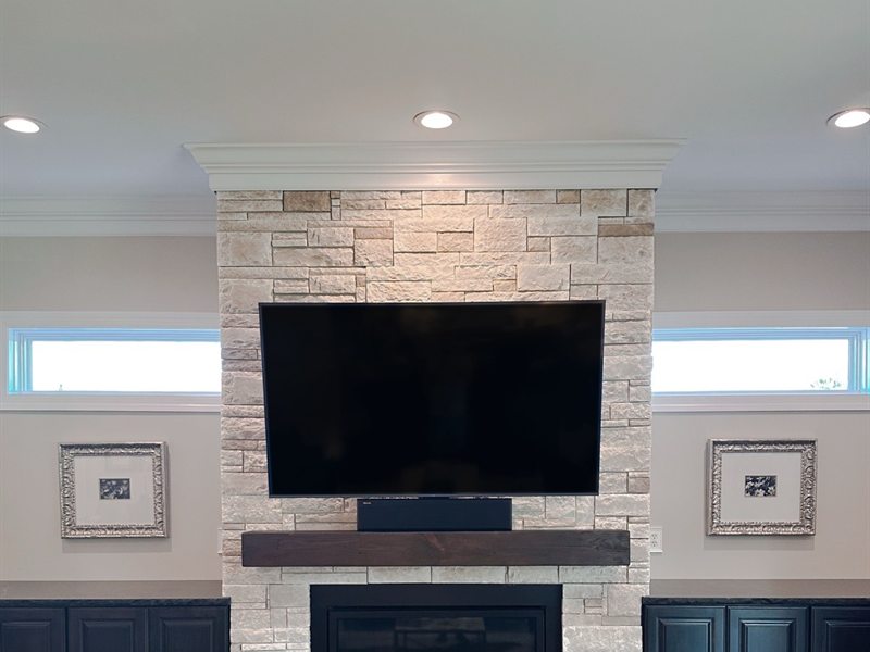 Large TV mounted on a stone fireplace above a wood mantel with a soundbar below
